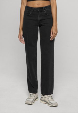 Jean droit en denim noir taille haute, design à cinq poches avec des détails de couture subtils. Porté avec des chaussures de sport grises.