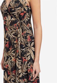 Robe florale avec un fond noir, présentant de grands motifs de feuilles en beige et rouge. Comprend un détail noué à la taille et une texture douce.