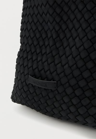 Μαύρη υφασμένη τσάντα με υφή στην επιφάνεια, που διαθέτει μια λεία μαύρη ετικέτα προσαρτημένη. Ο σχεδιασμός έχει δομημένο, στρογγυλό σχήμα.