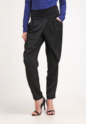 Osoba w czarnych, luźnych spodniach z wysokim stanem, w połączeniu z czarnymi sandałami na wysokim obcasie i niebieską bluzką z długim rękawem.