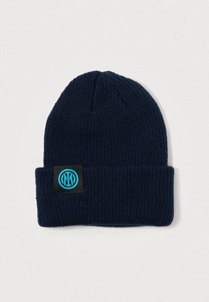 Marineblå strikket beanie lavet af blødt stof, med en foldet manchet og et sort mærke med et teal cirkulært logo.