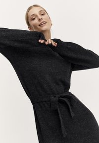 Abito nero in maglia con vita cintata, maniche lunghe e vestibilità morbida. Il tessuto ha una finitura testurizzata, che ne esalta l'aspetto casual.