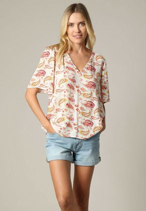 Blouse à manches courtes, décolletée en V, en tissu léger avec un motif paisley coloré en orange, rose et jaune sur un fond crème.