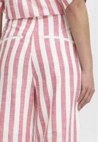 Linen trousers featuring vertical pink and white stripes, with a smooth texture, mid-rise fit, and two back pockets.