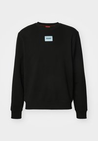 Sudadera negra con cuello redondo, mangas largas y un parche de logo rectangular azul con la palabra "HUGO" en el centro del pecho. Textura suave.