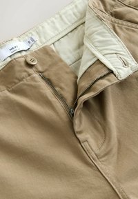 Chinos caqui con cierre de botón y cremallera, que cuentan con una textura de tejido suave y un forro interior en la cintura de color beige claro.