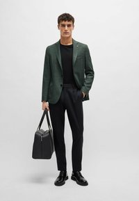 Blazer a quadri verdi, camicia nera, pantaloni neri su misura, scarpe in pelle nere e borsa nera. Texture liscia e design strutturato.