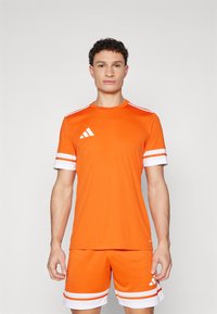 Orange athletic shirt with white stripes on sleeves, paired with matching shorts. Material appears lightweight; features Adidas logo design.