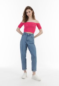 Lyserød strikket cropped top med bare skuldre og korte ærmer, parret med højtaljede lyseblå jeans og hvide sneakers.