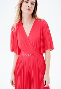 Vestido rojo plisado con mangas cortas y fluidas y un escote en V. Cuenta con una cintura ceñida con un detalle de hebilla de hardware plateado.