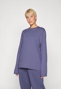 Langermet topp i lilla bomull, med rund hals, løs passform og brede ermer. Matchet med bunnen i lignende farge.