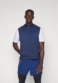 Gilet sans manches navy en tissu léger, avec un col haut et une fermeture éclair. Agrémenté d'une tirette de fermeture éclair rouge contrastante.
