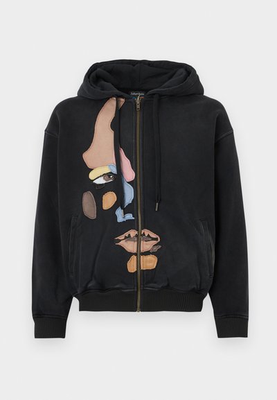 Black hooded sweatshirt with a zip front, featuring a colorful abstract face design made of textured fabric patches.
