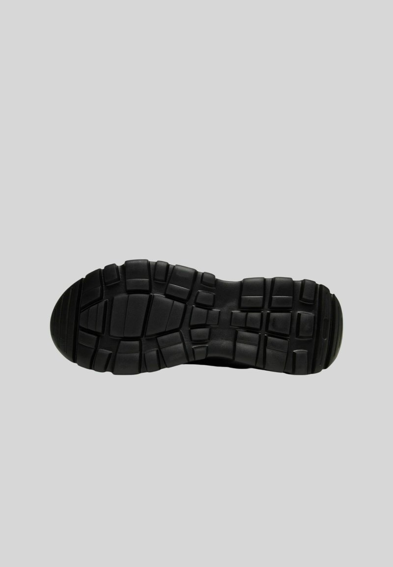 Semelle de chaussure de sport noire avec une surface en caoutchouc texturé, présentant des motifs de traction multidirectionnels pour une meilleure adhérence et stabilité.