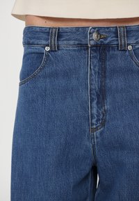 Blå denimjeans med rett snitt, fem lommer, kobbersting og sølvknapp-lukking i midjen.