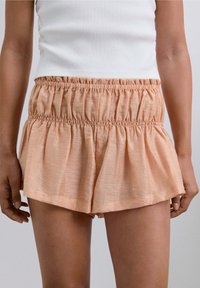 Pantalones cortos de melocotón claro con cintura elástica y textura fruncida. La tela es suave y ligera, con un diseño fluido.