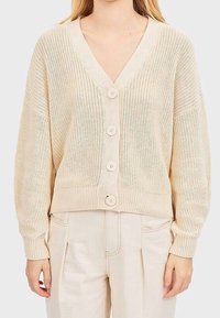 Cardigan beige en tricot avec col en V, doté de cinq grands boutons sur le devant et de poignets et ourlet côtelés. Tissu doux et texturé.