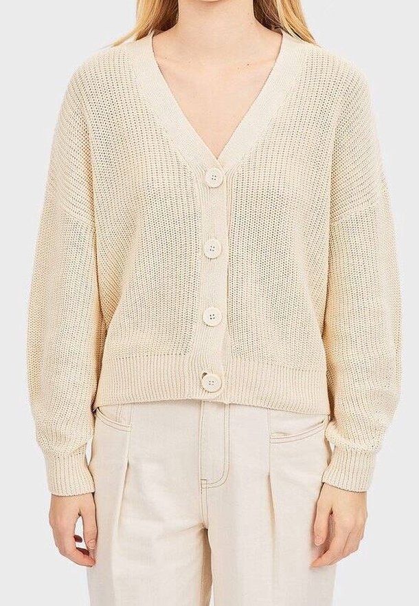 Cardigan beige en tricot avec col en V, doté de cinq grands boutons sur le devant et de poignets et ourlet côtelés. Tissu doux et texturé.