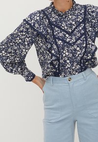 Námořnická květinová blůza s bílými květy, volánkovým límcem a rukávy, s vertikálními a horizontálními krajkovými detaily. Světle modré manšestrové kalhoty.