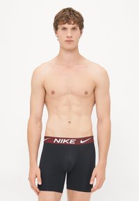Boxeri atletici negri, cu o talie burgundă ce prezintă logo-ul alb "Nike". Material neted, lungime până la mijlocul coapsei și design ajustat.