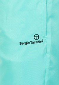 Lichtblauwe sportjas met een gladde textuur, zwart "Sergio Tacchini" logo en een subtiel ruitpatroon overal.