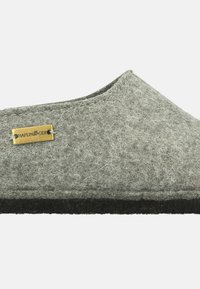 Gray felt slip-on shoe with black rubber sole, showcasing a simple design. Features a metal logo tag on the upper side.