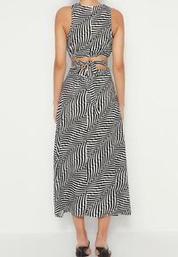 Svart och vit randig midiklänning med en figursydd crop top och knytning i ryggen, med ett geometriskt mönster och en flödande kjol.