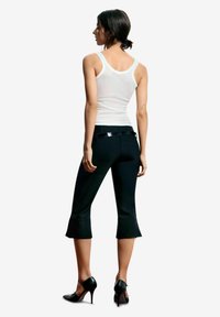 Zwarte cropped broek met uitlopende zoom, gemaakt van rekbare stof. Gecombineerd met een wit tanktopje en zwarte hoge hakken, voorzien van een glanzende riem.