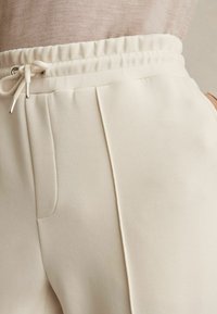 Pantaloni jogger dintr-un material moale, bej, cu talie elastică și șnur, buzunare laterale și detalii subtile de cusătură.