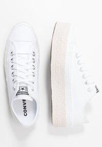 Sneakers bianchi in tela con suola in giuta intrecciata, dotati di occhielli in metallo, lacci bianchi e un logo nero sulla linguetta.