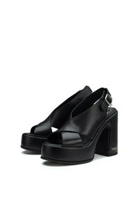 Tacchi a piattaforma in pelle nera con punta aperta e design con cinturino alla caviglia. Presentano audaci tacco a blocco e un dettaglio con fibbia alla caviglia. Texture liscia.