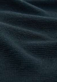 Gestructureerde donkerblauwe stof met een geweven patroon, die kleine, verhoogde ontwerpen toont. Het materiaal lijkt zacht en flexibel, en valt soepel.