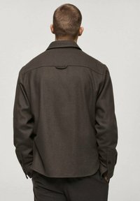 Brown woolen shirt jacket with a collar, button cuffs, and a back yoke detail. The fabric has a smooth texture and a slightly structured fit.