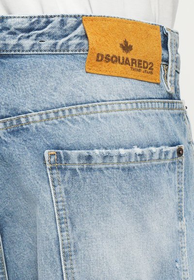 Ljust blå denimjeans med en texturerad gul läderlapp som har "DSQUARED2"-logotyp. Exponerad sömnad och subtila slitningar.