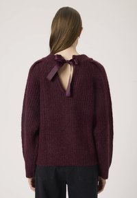 Maglione lavorato a maglia bordeaux con apertura a chiave sul retro e fiocco, maniche lunghe e un motivo testurizzato. Silhouette semplice e rilassata.