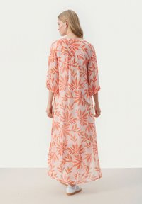 Lång, genomskinlig klänning i mjuk rosa med orange blomsterdesign. Har lösa ärmar och en flödande silhuett, med en avslappnad passform.