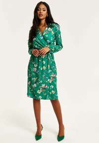 Green floral wrap dress with long sleeves, featuring a v-neckline and tied waist. The fabric is smooth with a glossy finish.