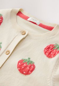 Cardigan en tricot crème avec des boutons en bois et des motifs de fraises rouges, avec un col côtelé et une étiquette "NEXT" à l’intérieur du col.