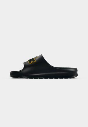 Sandale slide en caoutchouc noir avec un motif de fleur verte et jaune sur la bride, présentée sur un fond gris clair uni.