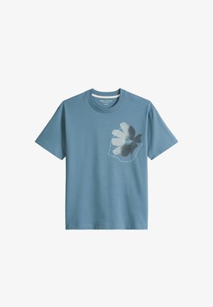 T-shirt bleu à manches courtes avec col rond, présentant un grand motif floral gris clair et foncé ainsi qu'un texte circulaire blanc sur la poitrine gauche.
