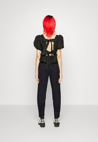 Svart blus med textur och puffärmar, öppen rygg som är knuten med sløjfer; tillsammans med marinblå rutiga byxor och silverfärgade platåskor.