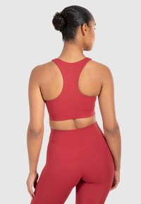 Top corto deportivo rojo con un diseño de espalda nadadora, hecho de material suave y elástico. Presenta una silueta ajustada y una coloración sólida.