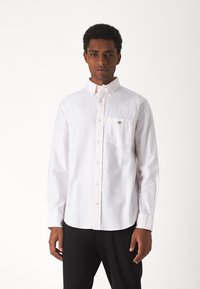 Camicia bianca a maniche lunghe con bottoni, caratterizzata da un sottile motivo a righe, una tasca sul petto e un colletto classico, realizzata in tessuto leggero.