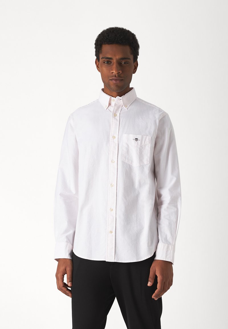 Camicia bianca a maniche lunghe con bottoni, caratterizzata da un sottile motivo a righe, una tasca sul petto e un colletto classico, realizzata in tessuto leggero.