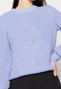 Suéter de punto color azul claro con un patrón texturizado de formas de diamante. Puños y dobladillo acanalados, cuello redondo y un corte holgado.