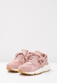 Par av rosa mockaskor för träning med vita mellansålar och yttersålar av gummigummi, visade på en vit yta mot en ljus bakgrund.