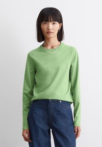 Langermige groene top van soepel materiaal, met een ronde hals en een ontspannen pasvorm, gecombineerd met donkerblauwe high-waisted jeans.