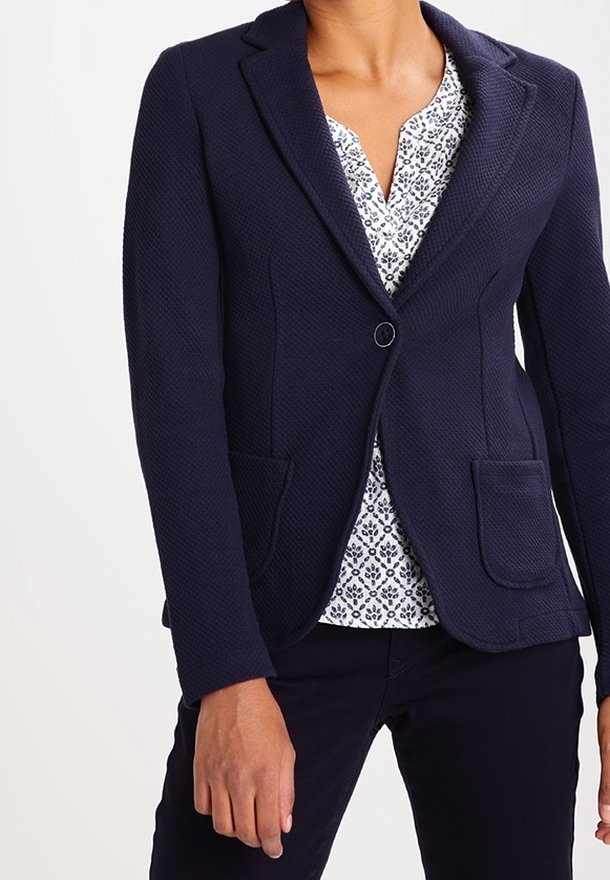 Námořnická texturovaná blazer s jedním knoflíkem, dvěma předními kapsami a klopovými límci, nošený přes vzorovanou blůzu.
