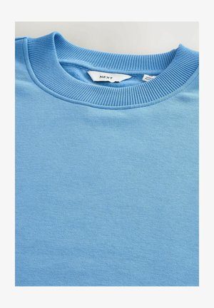 Svijetloplava dukserica s rebrastim okruglim izrezom. Ima mekanu teksturu, jednostavan dizajn i oznaku koja ukazuje na brend "NEXT."