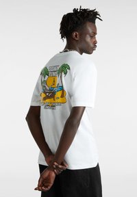 Hvid bomulds t-shirt med et farverigt grafisk motiv på ryggen, der viser et skelet, der slapper af under palmerne sammen med tekstelementer.